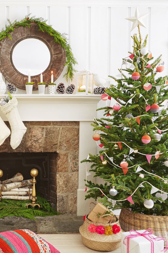 Weihnachtsbaum geschmückt mit bunten Christbaumkugeln und Girlanden aus Papier, Tannenzapfen und weiße Kerzen auf dem Kamin 