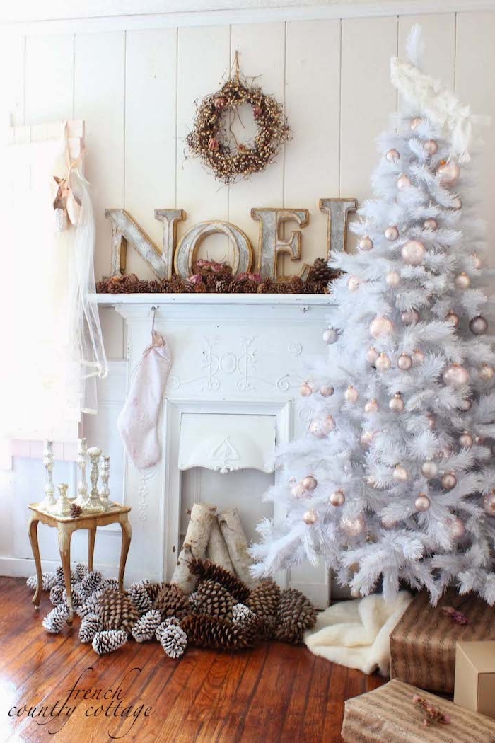 Weißer Weihnachtsbaum vor weißem Kamin, Zapfen am Boden, Weihnachtskranz und Weihnachtsstrumpf an der Wand