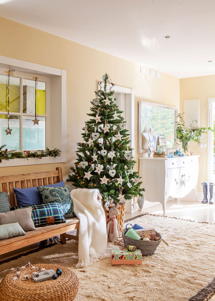 Echter Weihnachtsbaum geschmückt mit Sternen und Herzen, Dekokissen und weiße Deko auf Holzbank, Couchtisch aus Rattan 