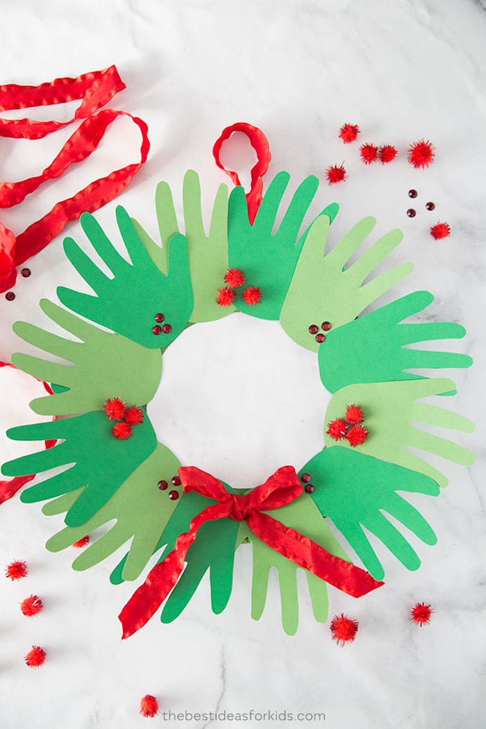 Weihnachtskranz aus grünem Karton selber basteln, Handabdrücke kleben, rote Schleife und Pompons