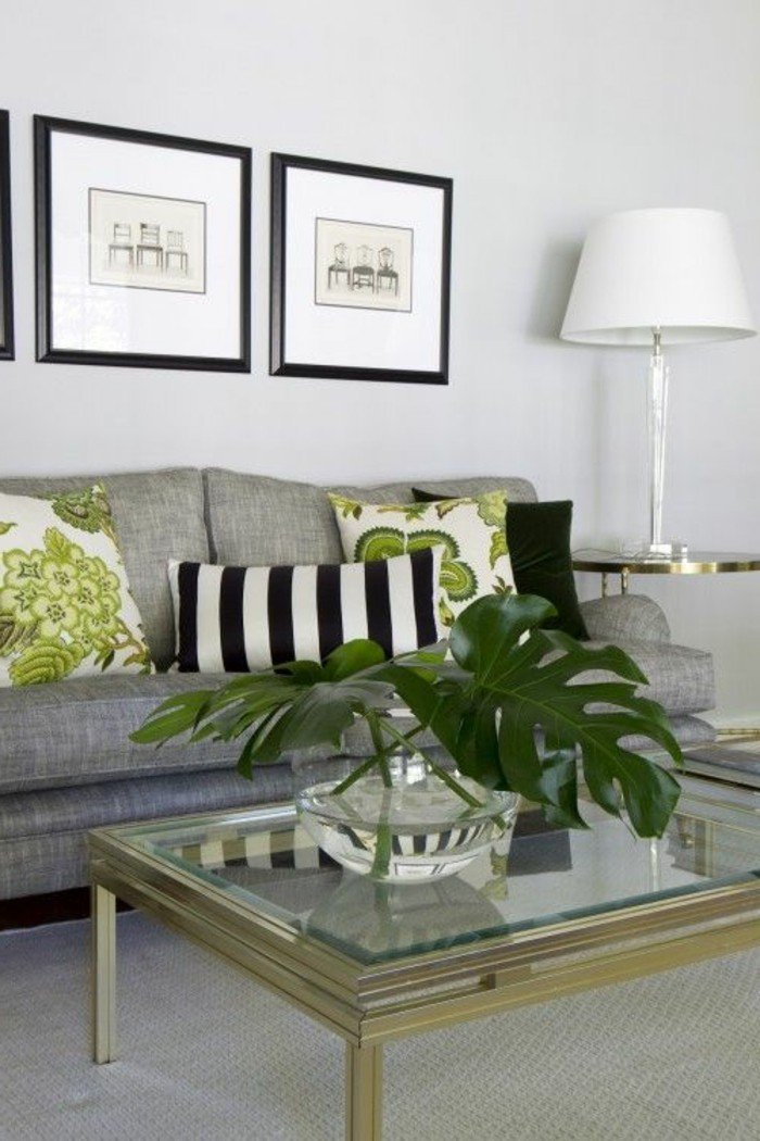 ein graues Sofa, grüne Kissen, Tisch aus Glas, eine Vase mit großen Blättern, Wohnzimmer Weiß Grau