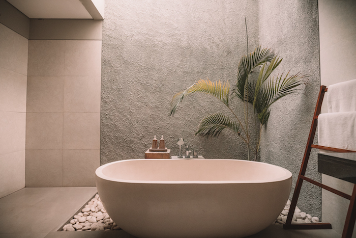 palme mit grünen blättern und eine kleine weiße freistehende badewanne und ein boden mit weißen steinen, outdoor dusche