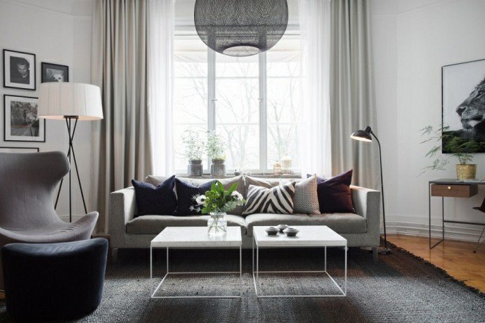 Wohnzimmer in Weiß Grau, ein weißes Sofa, ein grauer Sessel, zwei weiße Couchtische, schwarzer Lampenschirm
