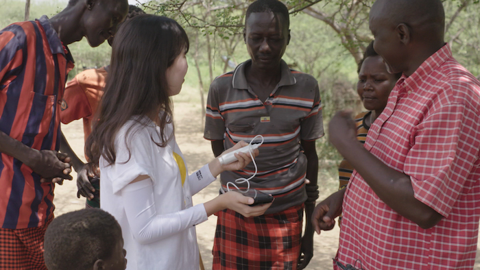 das solarkuh projekt, afrikanische eltern und eine junge frau mit einem weißen hemd und einem kleinen solarmodul