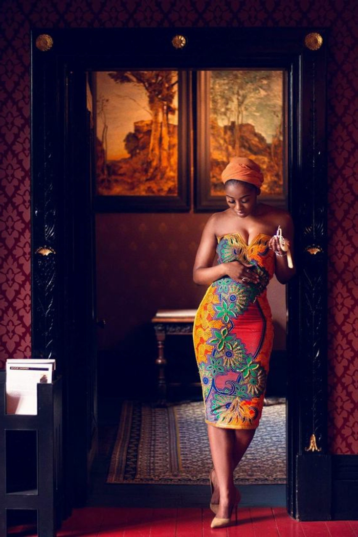 afrikanische kleider zum inspirieren, ein bild von einer frau im luxuszimmer, die model trägt buntes afrokleid und orangenes kopftuch