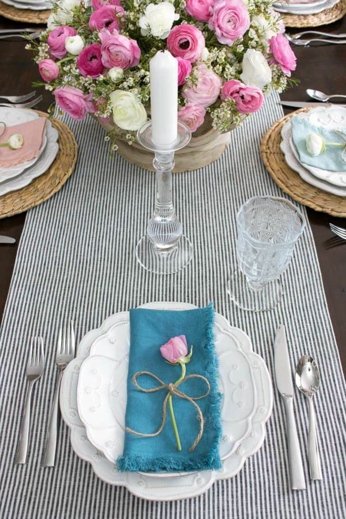 zwei weiße Teller, eine blaue Serviette, rosa Blumen, ein schwarz weißer Tischläufer, eine weiße Kerze, Geburtstagsdeko
