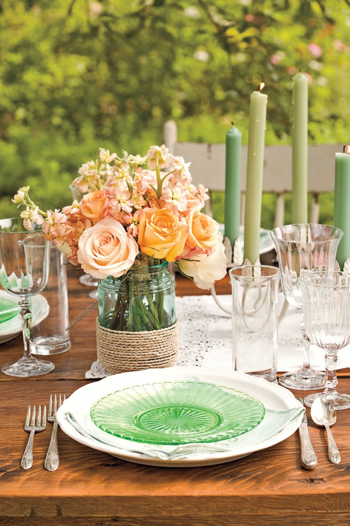 viele grüne Kerzen, orange Rosen in rustikale Vase, Teller aus Glas, ein Tisch aus Holz, Geburtstagsdeko