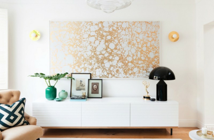 Wandgestaltung für Wohnzimmer, ein großes Bild mit goldfarbene abstrakte Motive, ein weißes Regal, schwarze Tischlampe