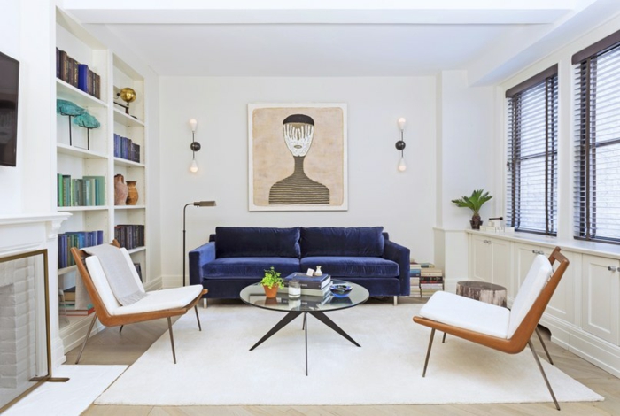 ein weißer Teppich, ein blaues Sofa, ein kleiner runder Tisch aus Glas, zwei Sessel, weiße Wandfarbe