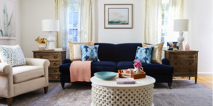 blaues Sofa, ein runder Tisch, ein grauer Teppich, ein weißer Sessel, Wohnzimmerwand mit Wandbilder
