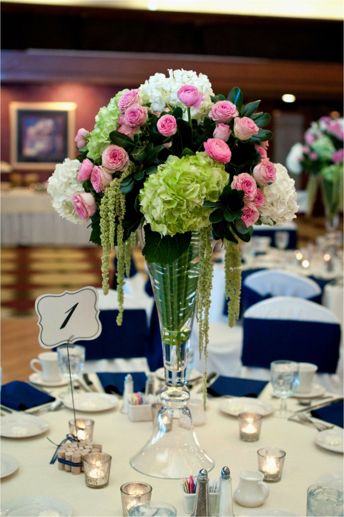 eine Vase aus Glas, rosa und weiße Blumen, weiße Tischdecke, kleine Windlichter mit Teelichter