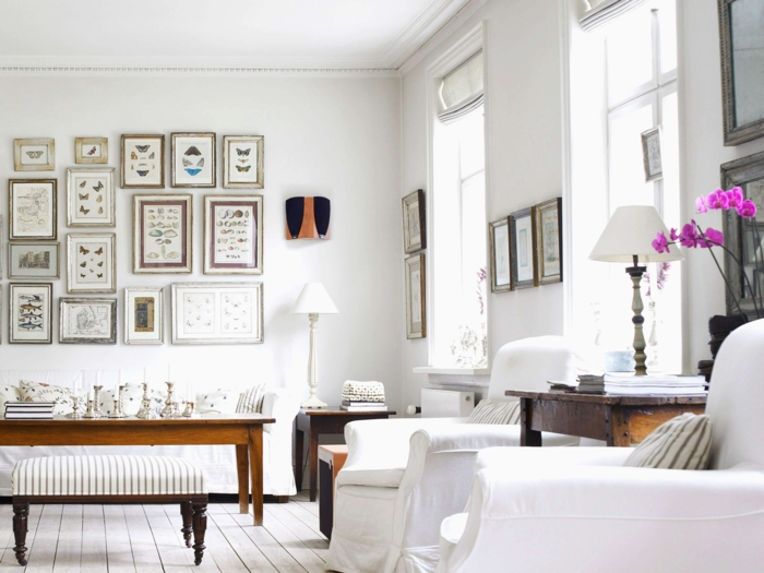 eine Menge Wandbilder, ein Tischlein aus Holz, zwei Sessel, weiße Diele, Wohnzimmerwand