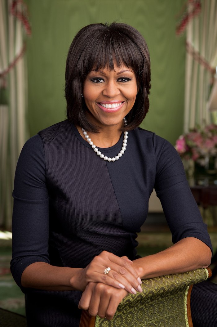 Michelle Obama Hairstyle, Stufenschnitt mit geradem Pony, glatte schwarze Haare, schwarzes Kleid und Perlenkette 