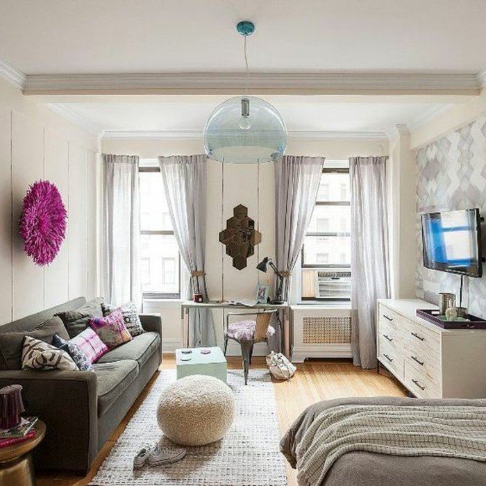 ein graues Sofa, bunte Kissen, ein runde lila Bild, ein weißer Teppich, lila Vorhänge, weißer Hocker, Wohnzimmer Ideen für kleine Räume
