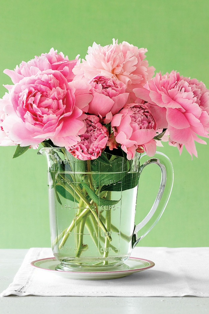 Blumen Tischdeko im Glas, rosa Rosen, eine Kanne voller Wasser, grüner Hintergrund, weißes Tuch