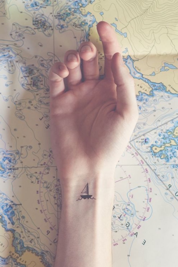 mini tattoos ideen, ein kleines schiff auf der hand, handgelenl , eine hand liegt auf weltkarte