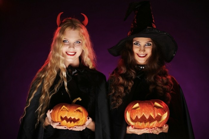 halloween kostüme und ideen, zwei frauen wie hexen verkleidet, schwarze mäntel, kürbis leuchten,, dunkellila hintergrund