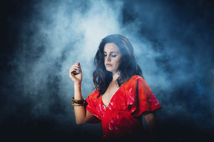 Lana Del Rey in rotem Kleid mit weiten Ärmeln, schwarze wellige Haare, matter Lippenstift und schwarzer Eyeliner 