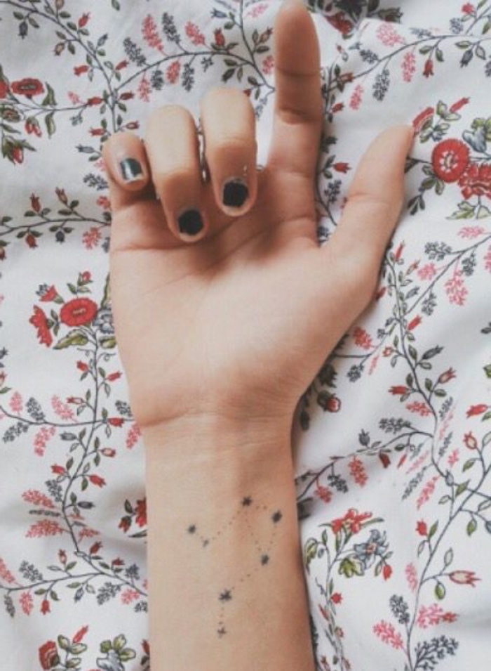 tattoo unterarm frau, schwarze kleine nägel, hand auf einem bunten stoff gelegt
