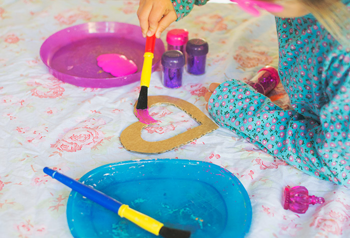 Bastelideen für Kinder, ein kleines Mädchen malt in rosarot ein ausgeschnittenes Herz aus Karton, Lila Teller, Blauer Teller