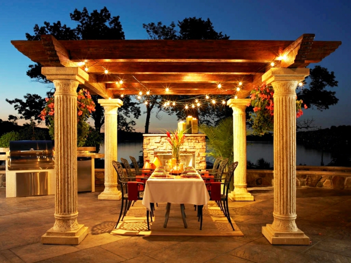 ein Garten voller schöne Lichter, ein für Party gedeckter Tisch, Säulen und ein Kamin, Gartengestaltung Ideen