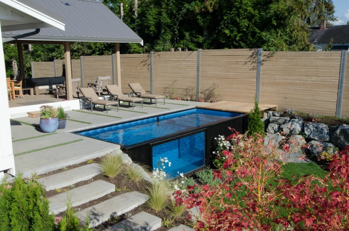 ein Schwimmbad mit klarem blauem Wasser, rote Blumen, drei Liegestühle, Garten gestalten, Treppen