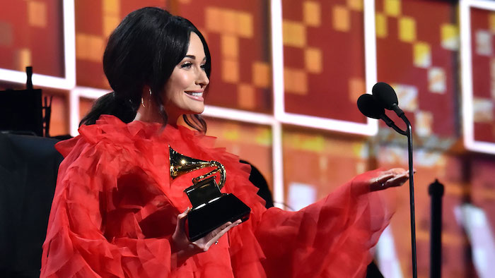 Kacey Musgraves bei den Grammys 2019, rotes Kleid mit langen Ärmeln, schwarze Haare, niedriger Zopf