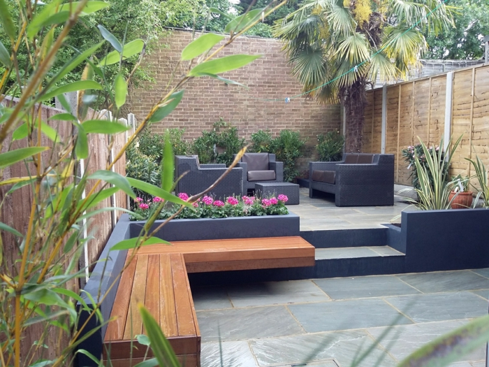 graue Fliesen, zwei Bänke, schwarze Loungemöbel, rosa Blumen, Hoher Sichtschutz, Gartengestaltung Beispiele