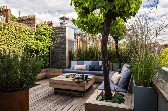 blaue Kissen, ein Tisch aus Holz, Terrassendiele, viele Bäume, ein Tischlein, Vasen, Gartengestaltung modern