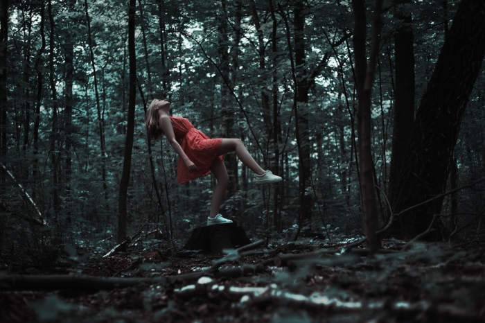 ein Mädchen mit einem roten Kleid in einem dunklen Wald, als ob sie ein Baum wäre, Bilder modern