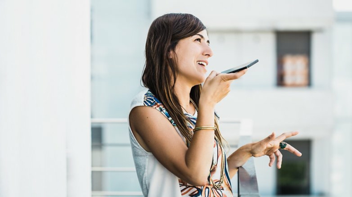 eine Frau gibt Sprachbefehle des Smartphones, als ob sie damit spricht, Google Assistant