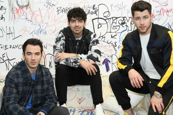 die drei Jonas Brothers, sitzen in einem Raum mit Graffiti, die Band sind wieder zusammen