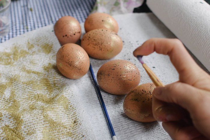 Kreative Techniken zum Ostereier färben, mithilfe eines Pinsels mit goldener Farbe bespritzen 