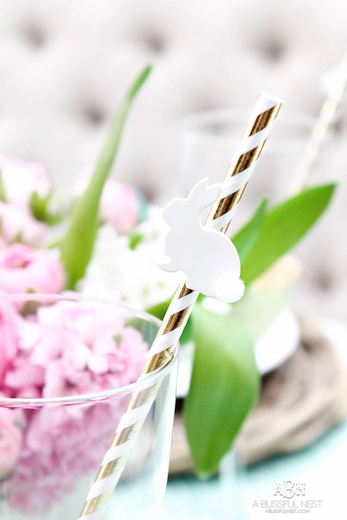Tischdeko für Ostern, kleiner weißer Osterhase an Strohhalm, rosa Hyazinthen im Hintergrund 