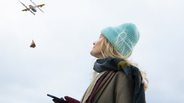 eine Frau mit blauem Mütze und blondem Haar hat durch App bestellt und jezt wartet sie auf die Drohne, Wing Drohnen