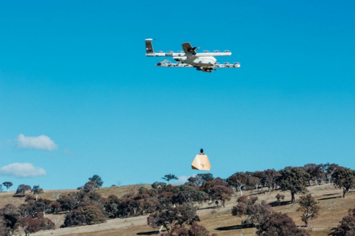 eine Drohne von Wing Drohnen fliegt über einen Hügel, ein Paket ist fertig für Lieferung