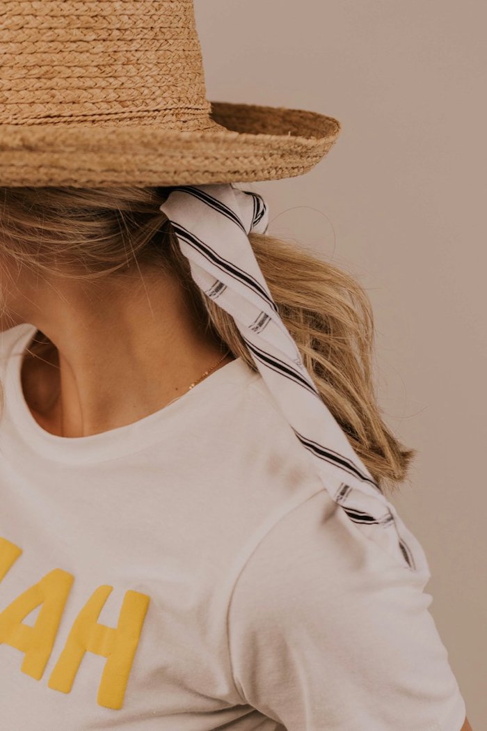 Sommerhut und gestreiftes Kopftuch, weißes Top mit gelber Aufschrift, lange blonde Haare 