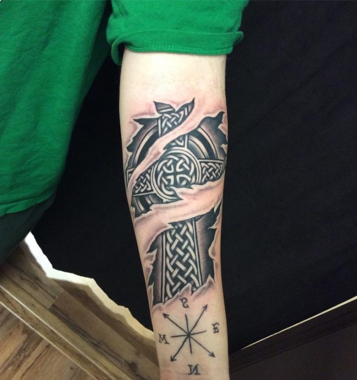 eisernes kreuz tattoo in schwarz und grau am arm, zerrissene haut, keltische motive, kompass am unterarm