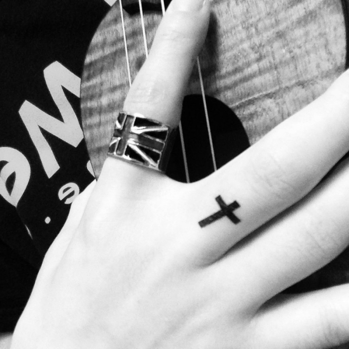 finger tattoo frau, großer ring, kleines motiv, tätowierung am mittelfinger, schwarzes kreuz, frauenhand