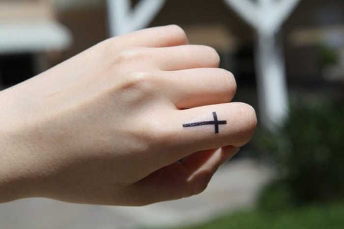 finger tattoo frau, kleine motive für frauen, schwarzes kreuz am zeigfinger, hand, frauenhand