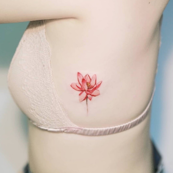 frau mit lotus tattoo an der körperseite, rote lotusblume, rote lotusblüte, kleines motiv