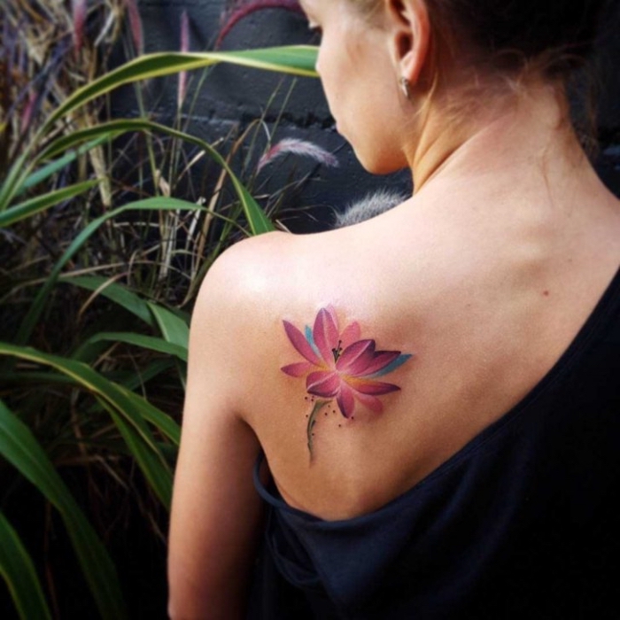 symbol für neuanfang, frau mit farbigeer tätowierung am rücken, rosa lotus, wasserfarben blume