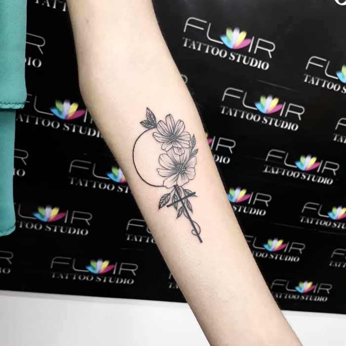 tattoo motive klein, kreuz in kombination mit kreis und blumen, schwarz graue tätowierung am arm