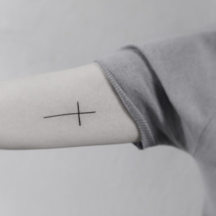simple tätowierung mit kreuz als motiv am arm, tattoo motive klein, oberarm tattoo frau