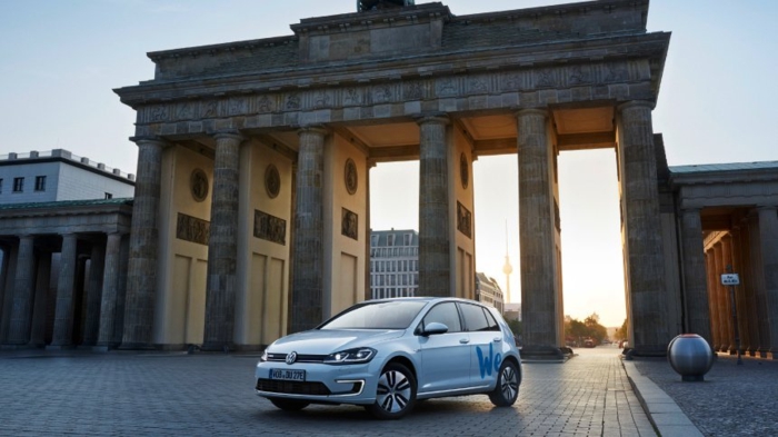 ein graues Auto hinter dem Brandenburger Tor, mit dem Logo von WeShare von Volkswagen