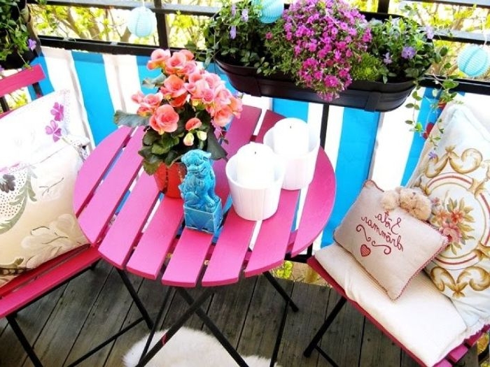 balkon dekorieren, ideen zum entlehnen, ein rosaroter tisch mit blumen darauf, lila hängeblumen, stühle mit kissen deko