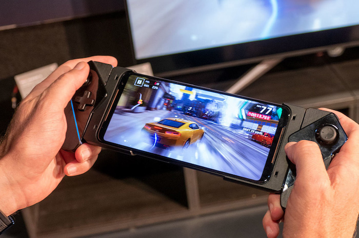 zwei hände eines spielers mit einem grauen smartphone Asus ROG Phone mit integriertem und modularem zubehör, ein spiel mit autos