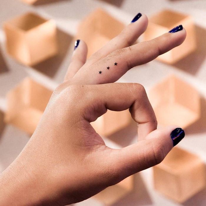 Zartes winziges Finger Tattoo, drei kleine Sterne am Mittelfinger, dunkelblauer Nagellack 