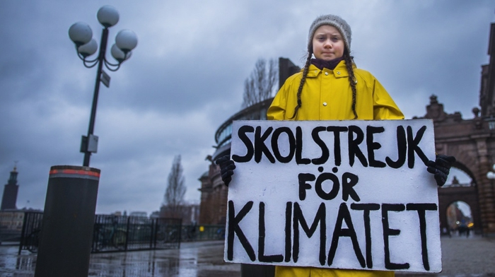Greta Thunberg, gelbe Jacke, graue Mütze auf einem Platz im Winter beim Regen