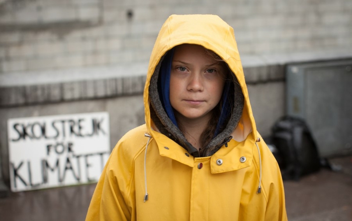 Greta Thunberg in einer gelben Jacke, im Hintergrund eine Tabelle mit Aufschrift Freitag für Zukunft